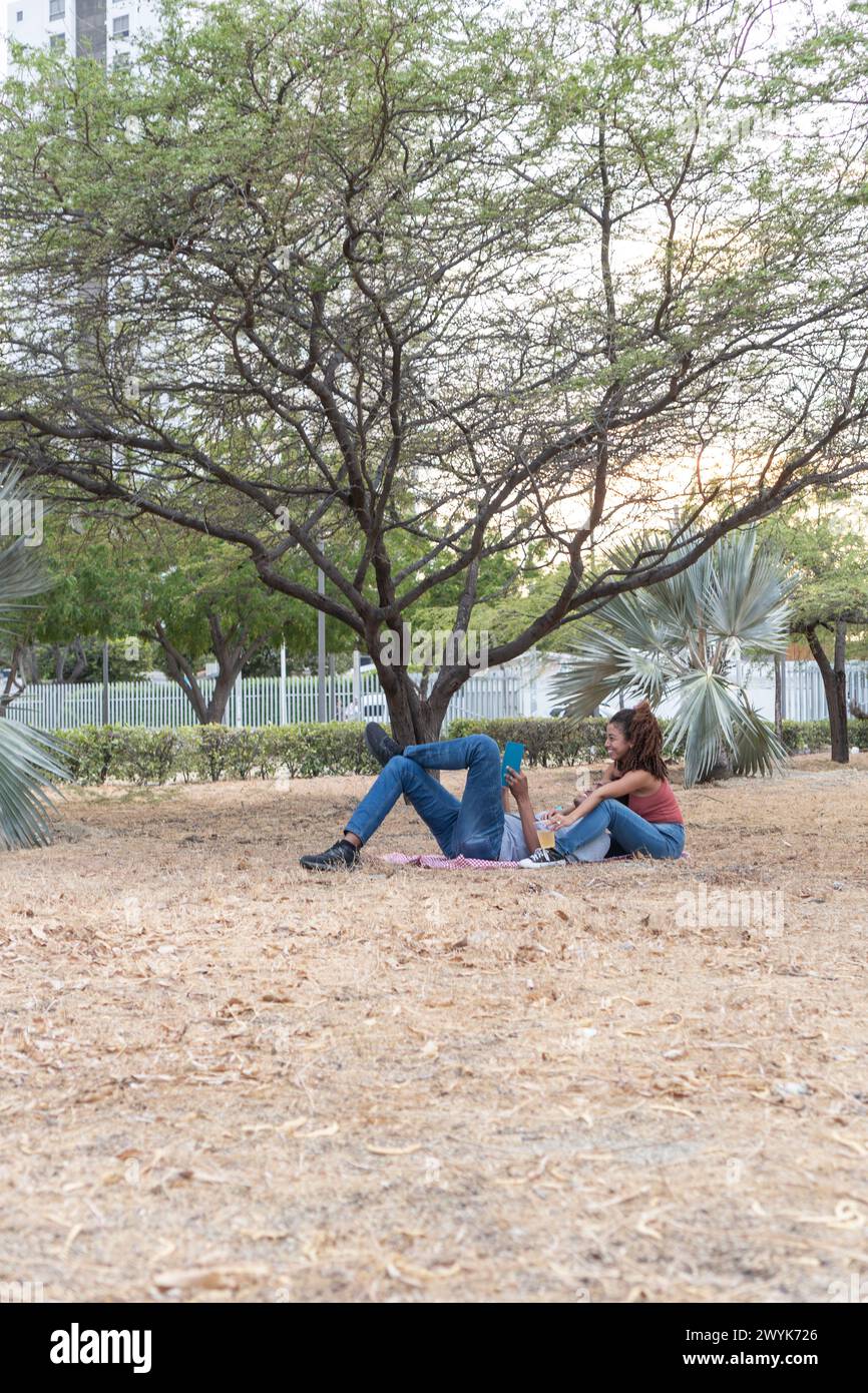La coppia si diverte a fare un picnic sereno al tramonto sotto gli alberi. Foto Stock