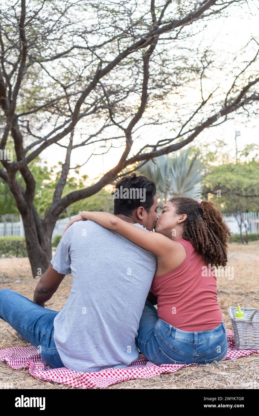 Un bacio romantico condiviso tra una coppia al tramonto, incorniciato da alberi. Foto Stock