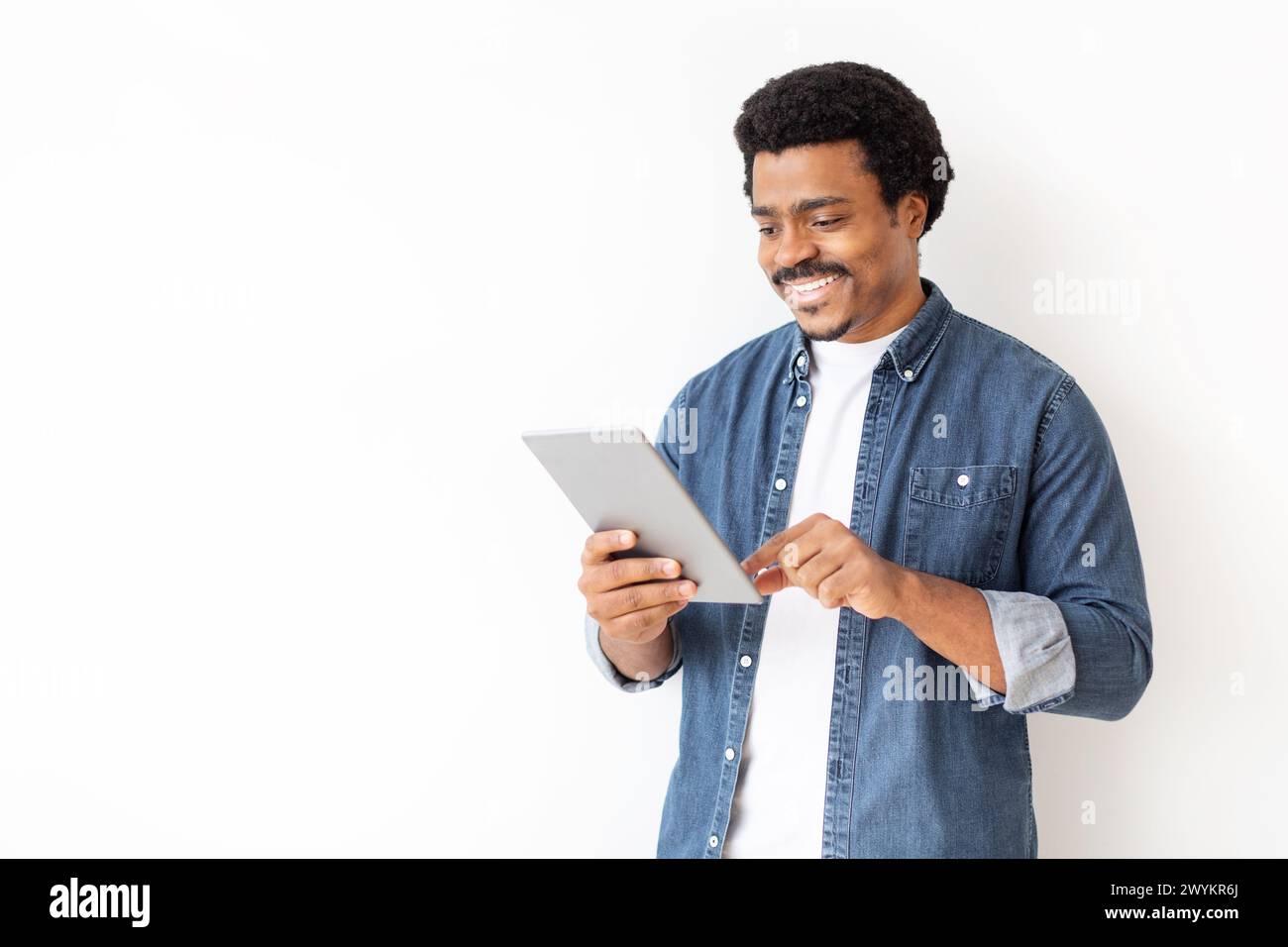 Contenuto uomo nero in camicia in denim coinvolgente con tablet digitale Foto Stock