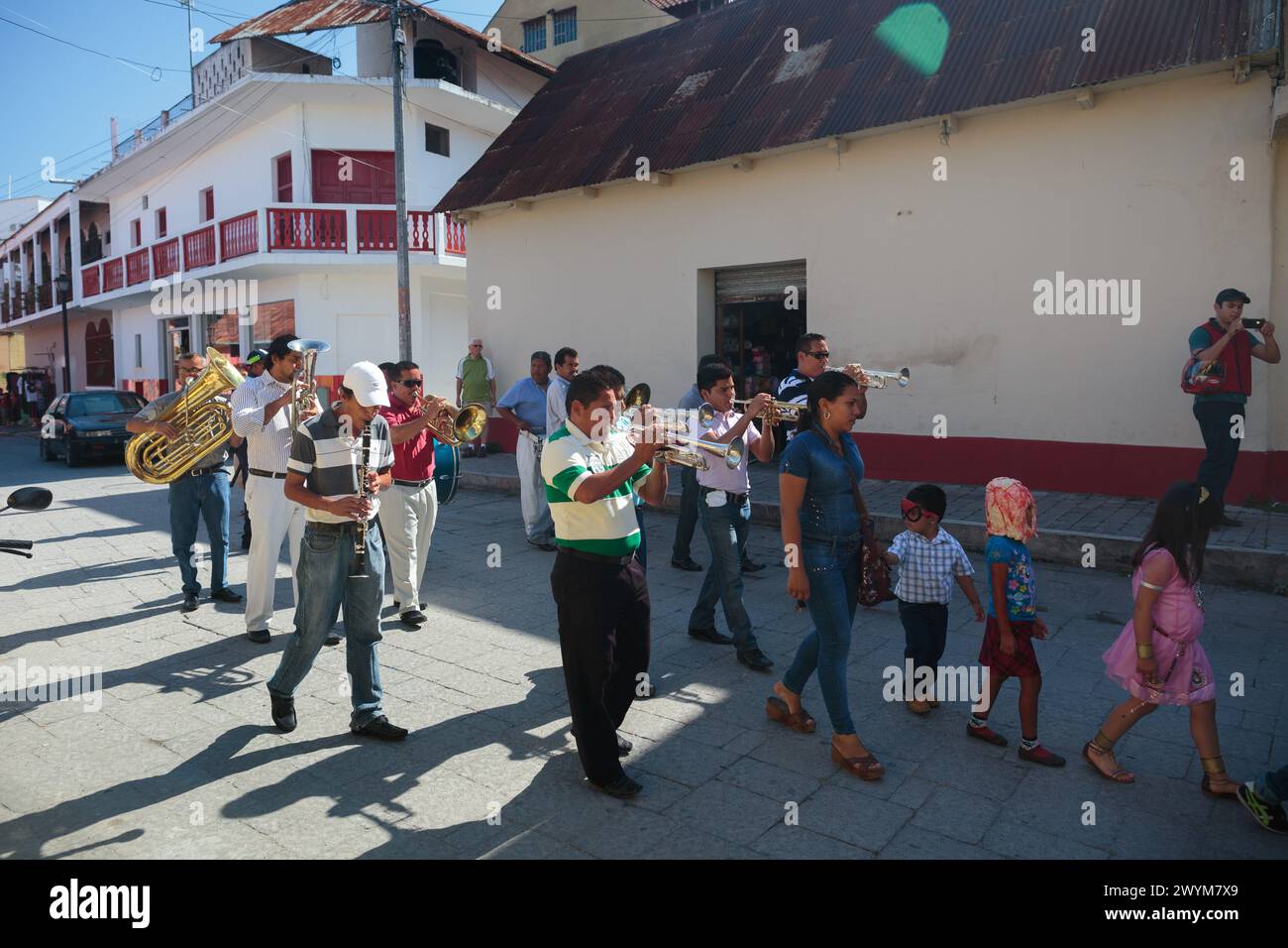 Una sfilata a piedi con bambini mascherati e trombettisti passeggiano per le strade di Flores nel nord del Guatemala, quartiere di Peten. Foto Stock
