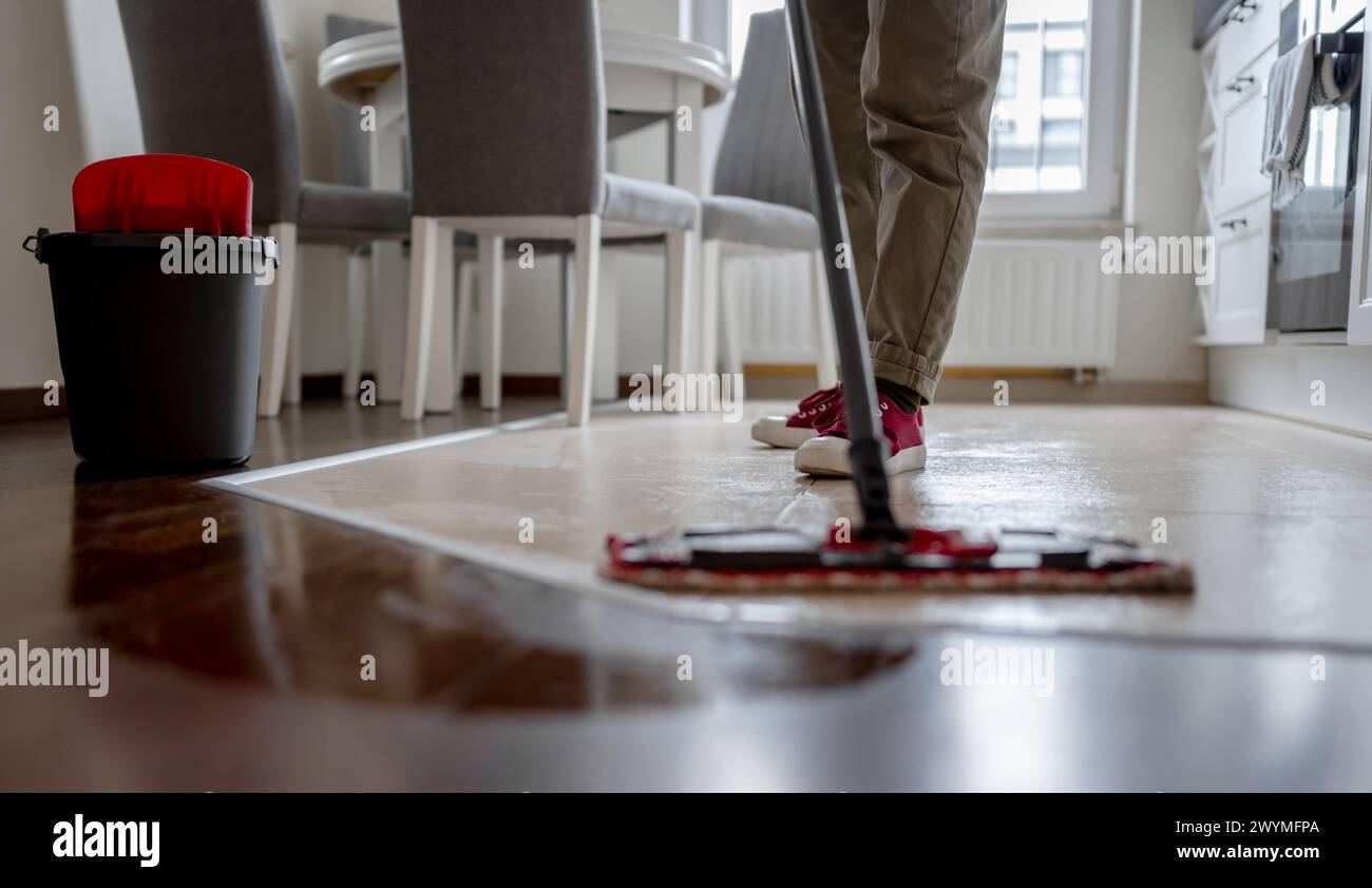 Woman Mops Floor in Kitchen with Broom prominente in primo piano Foto Stock