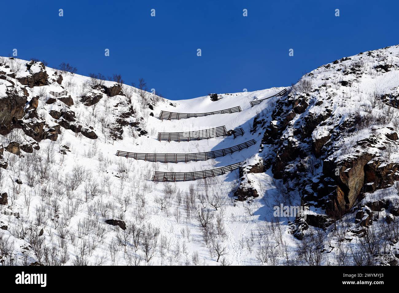 Recinzioni di Avalance sulla cima di una collina sopra la piccola città di Øksfjord a Finnmark, nel nord della Norvegia, nel soleggiato pomeriggio di marzo del 2024. Foto Stock