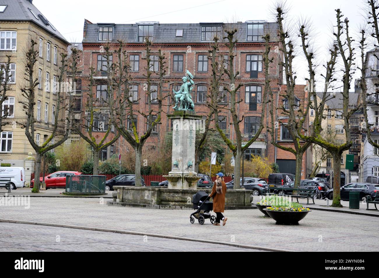 Una donna spinge un passeggino in una piazza con una statua storica nel quartiere Frederiksberg di Copenhapen, Danimarca, Europa Foto Stock