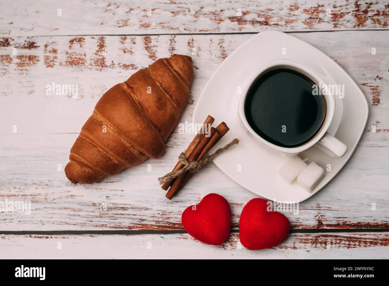 Tazza di caffè con croissant e cuori su un tavolo di legno. Concetto di colazione mattutina il giorno di San Valentino. Disposizione piatta, vista dall'alto Foto Stock