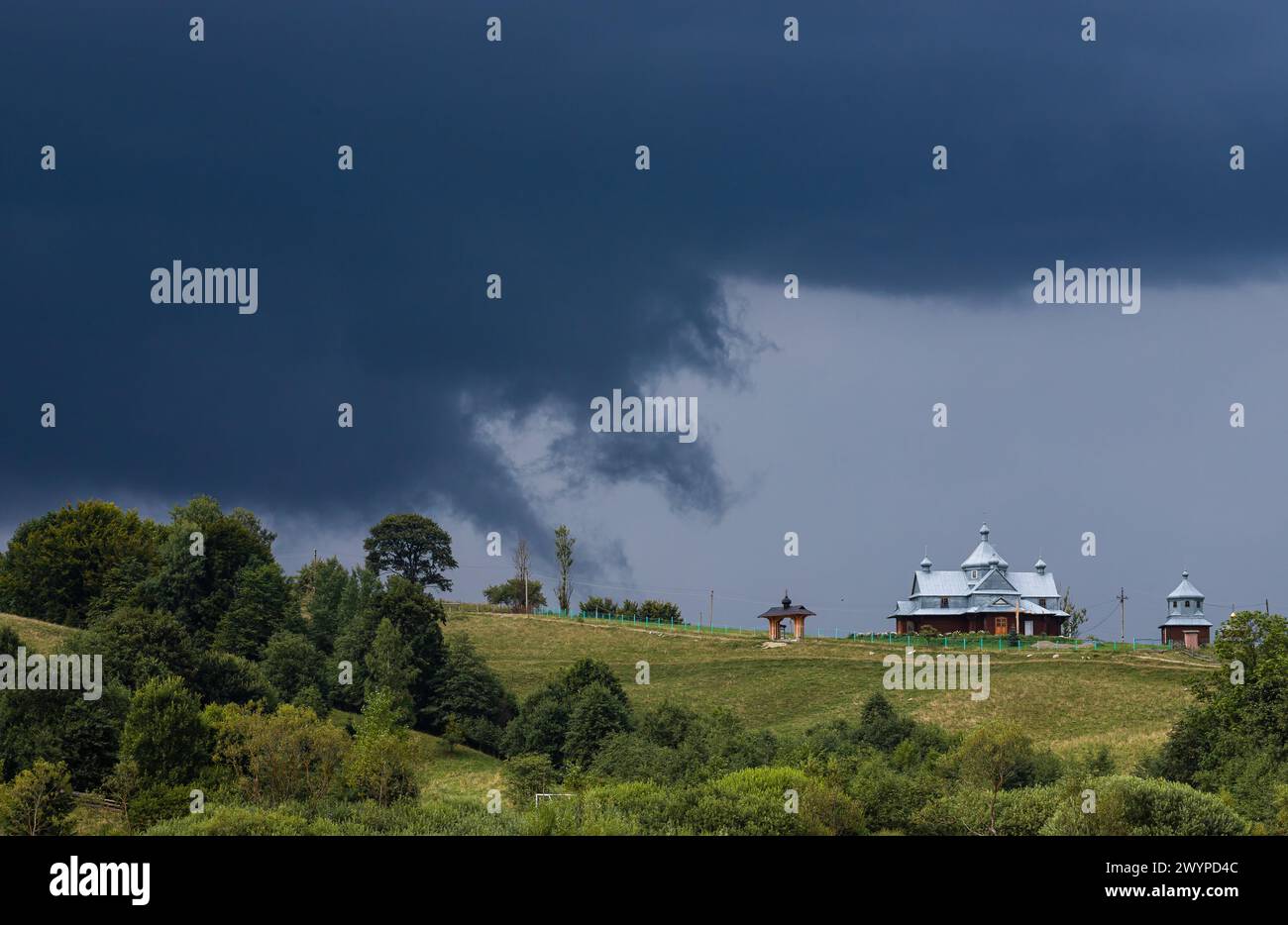 Nuvole tempesta, cielo minaccioso, collina e chiesa, alberi verdi prima della pioggia. Foto Stock