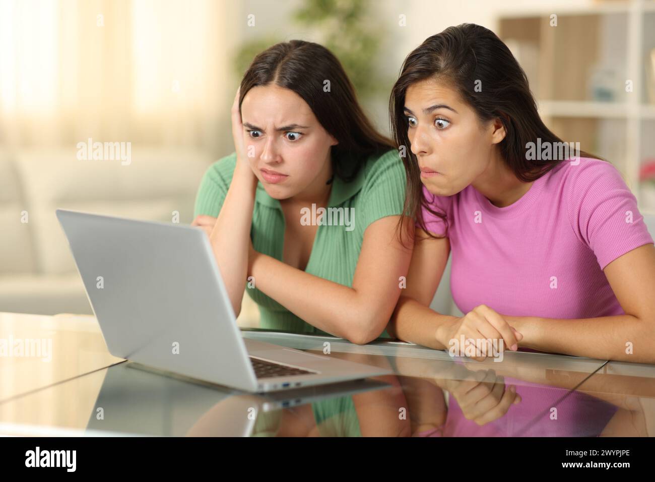 Amici perplessi che guardano contenuti multimediali assurdi su un notebook seduto a casa Foto Stock