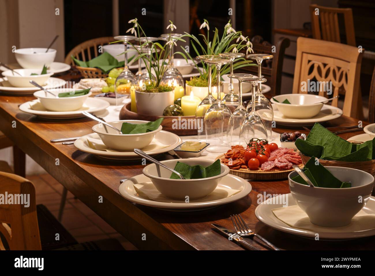 Cena per famiglie e amici su un grande tavolo di legno con varie sedie vintage, ambiente festivo con stoviglie, bicchieri da vino e decorazioni, d Foto Stock