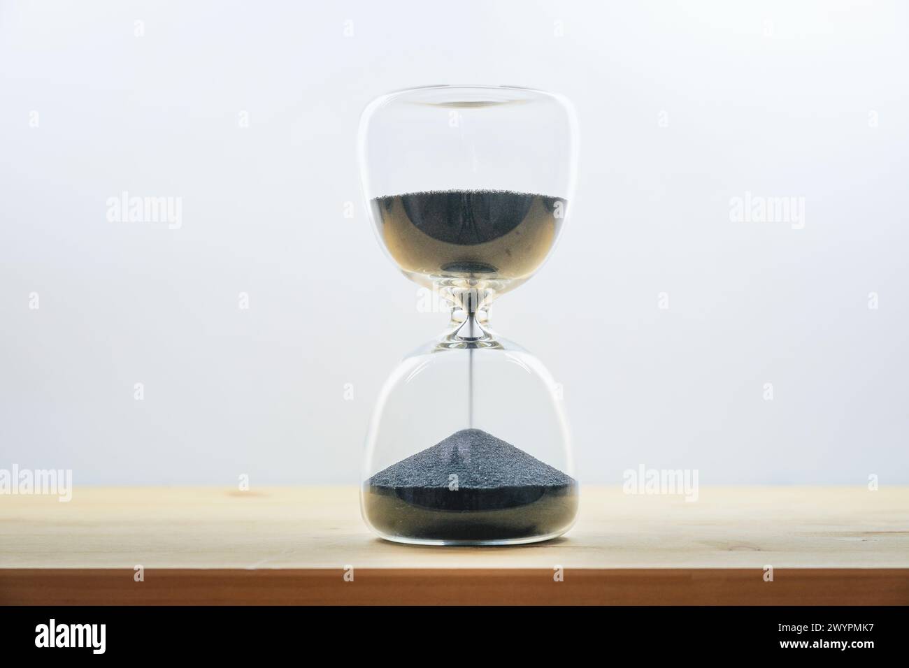 Clessidra con sabbia nera su un tavolo di legno su sfondo grigio chiaro, concetto di tempo che passa, cogli la giornata e goditi il momento, copia spa Foto Stock