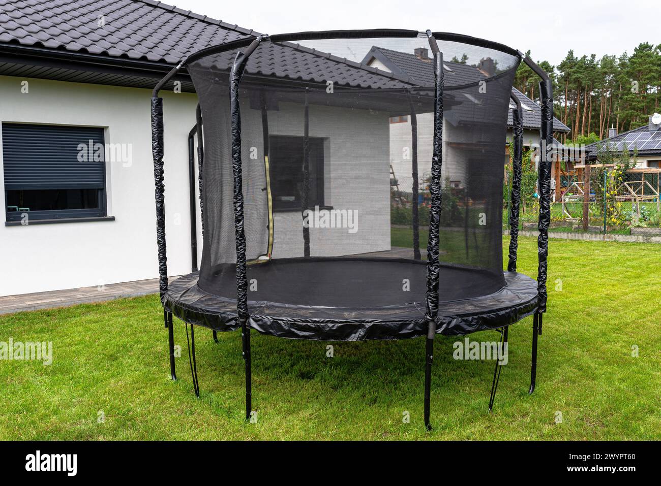 Grande trampolino da salto per bambini con rete protettiva e cerniera chiusa, in piedi in giardino. Foto Stock