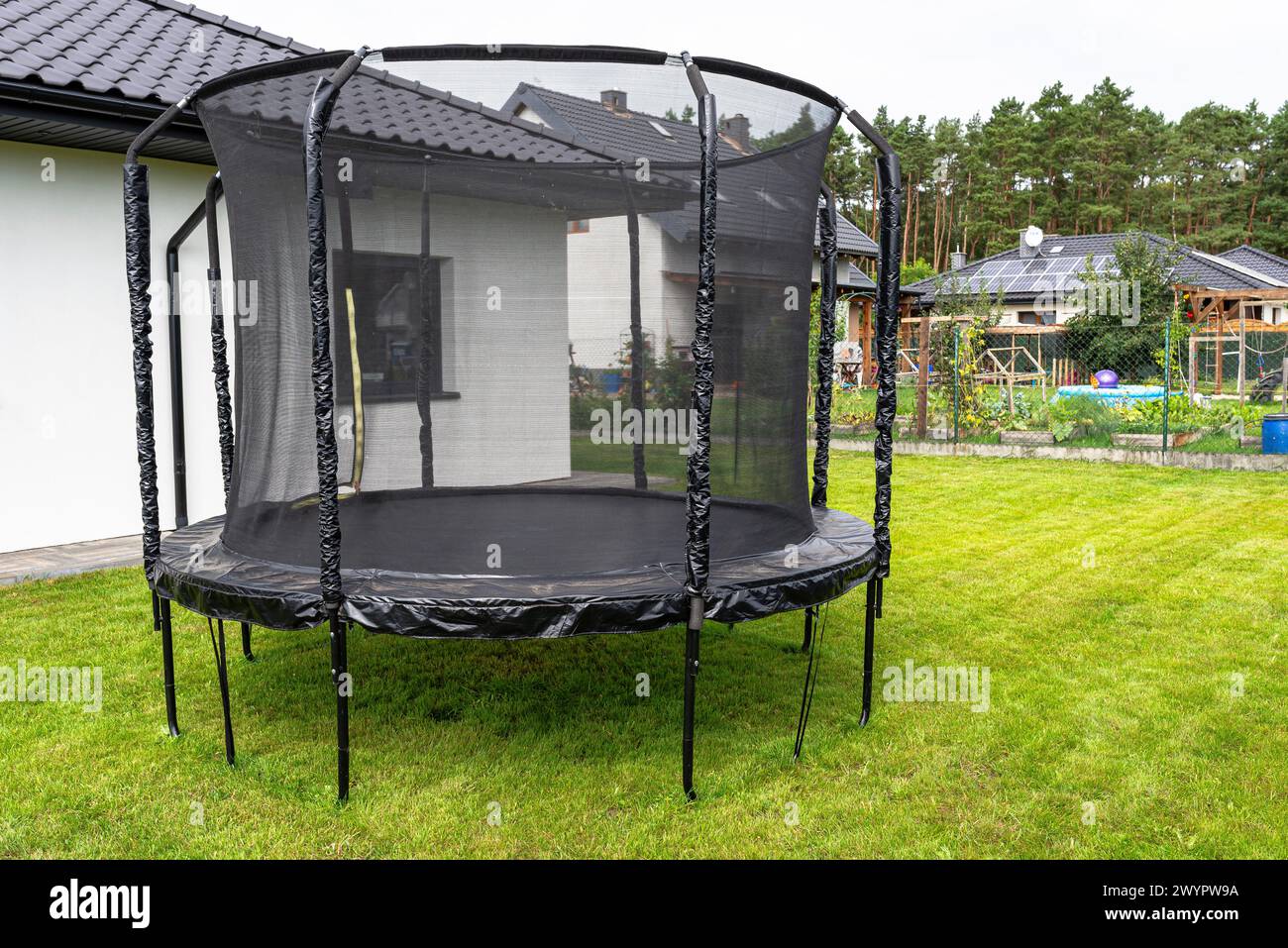 Grande trampolino da salto per bambini con rete protettiva e cerniera chiusa, in piedi in giardino. Foto Stock