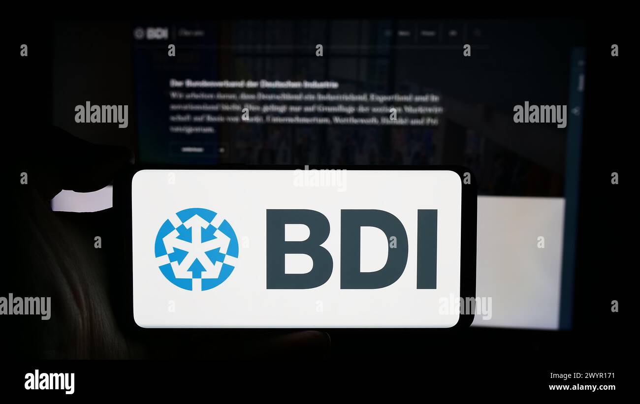 Persona che detiene un cellulare con il logo della Bundesverband der Deutschen industrie e.V. (BDI) davanti alla pagina web. Mettere a fuoco il display del telefono. Foto Stock