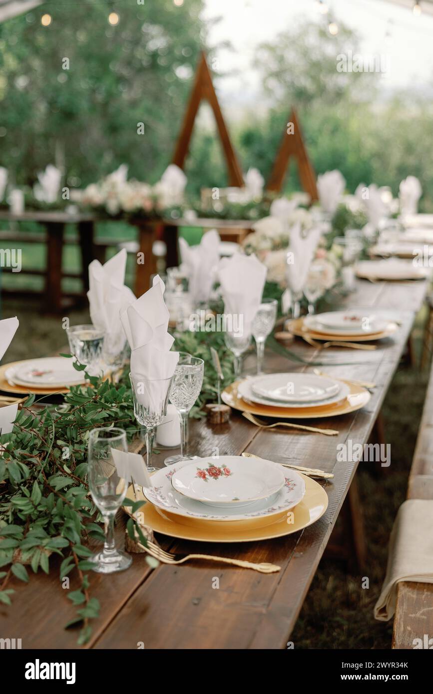 Tavolo per matrimoni all'aperto con vegetazione lussureggiante e dettagli dorati Foto Stock