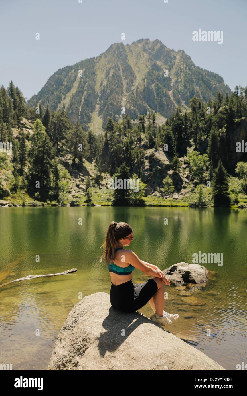 Ragazza seduta in un lago con una foresta e una montagna sullo sfondo Foto Stock