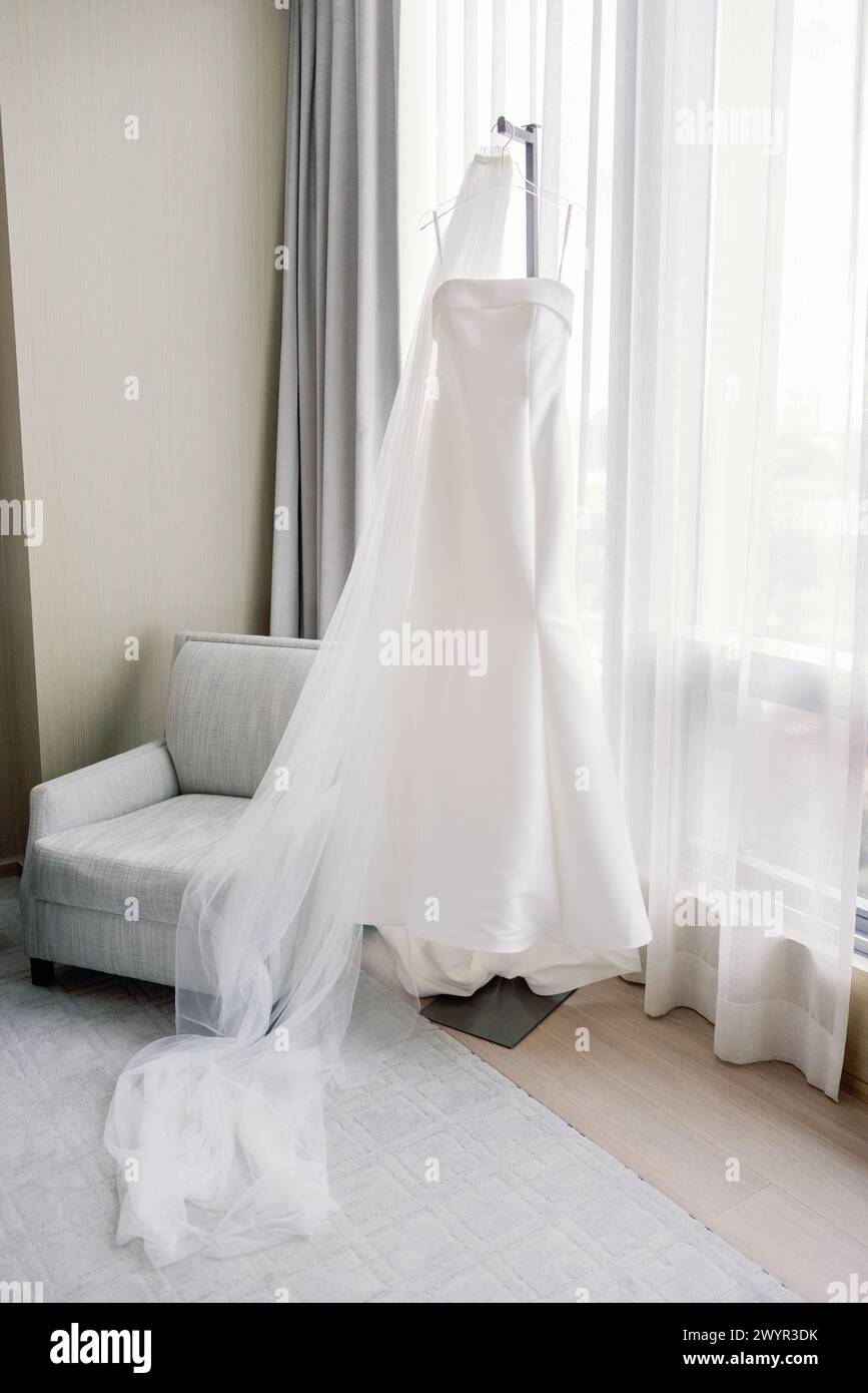 Moderno abito da sposa appeso con velo e luce naturale Foto Stock