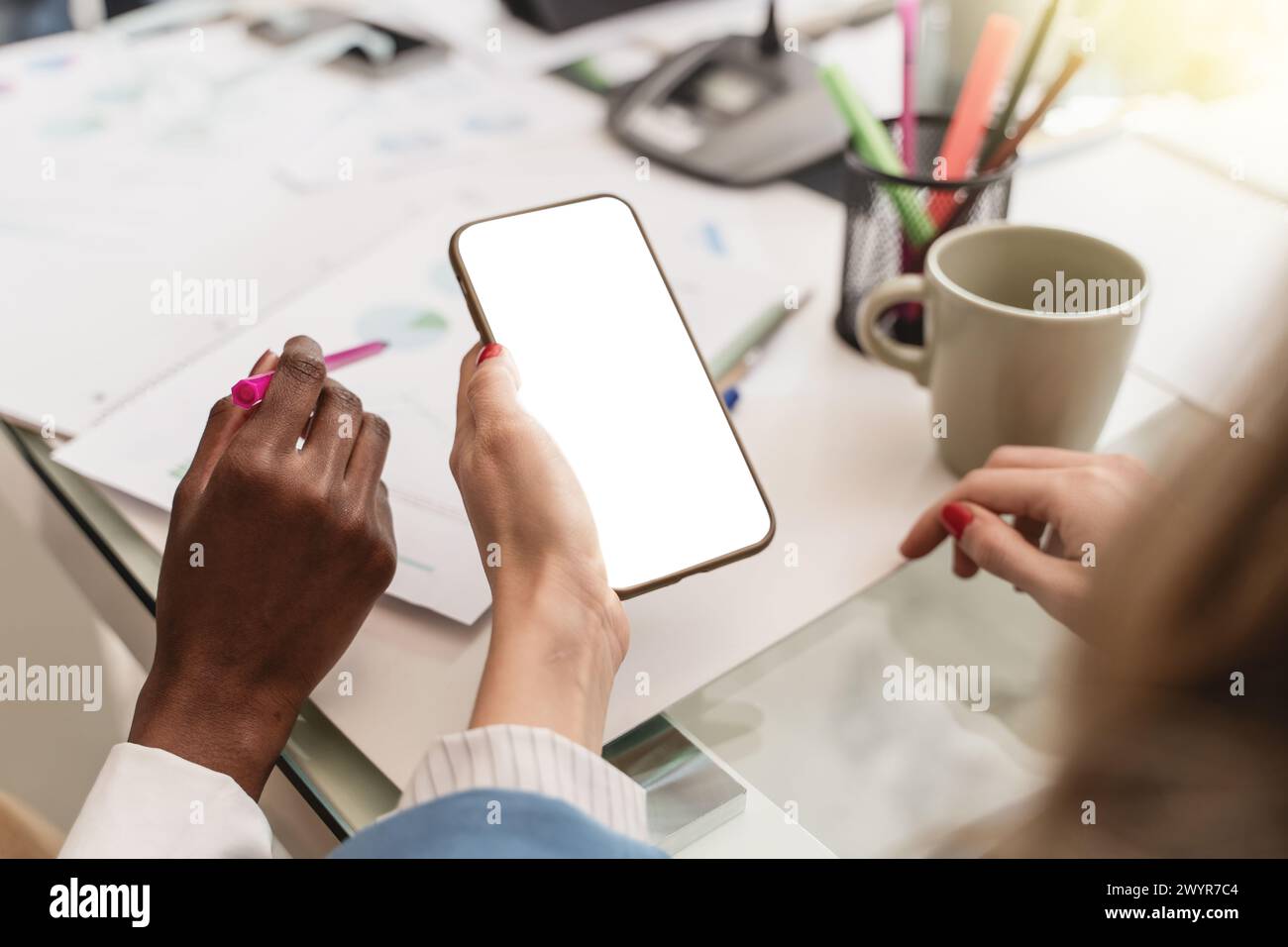 Due donne d'affari, africane e caucasiche, interagiscono con uno smartphone mockup screen, ideale per mostrare app diverse, dalle statistiche aziendali alle donne Foto Stock