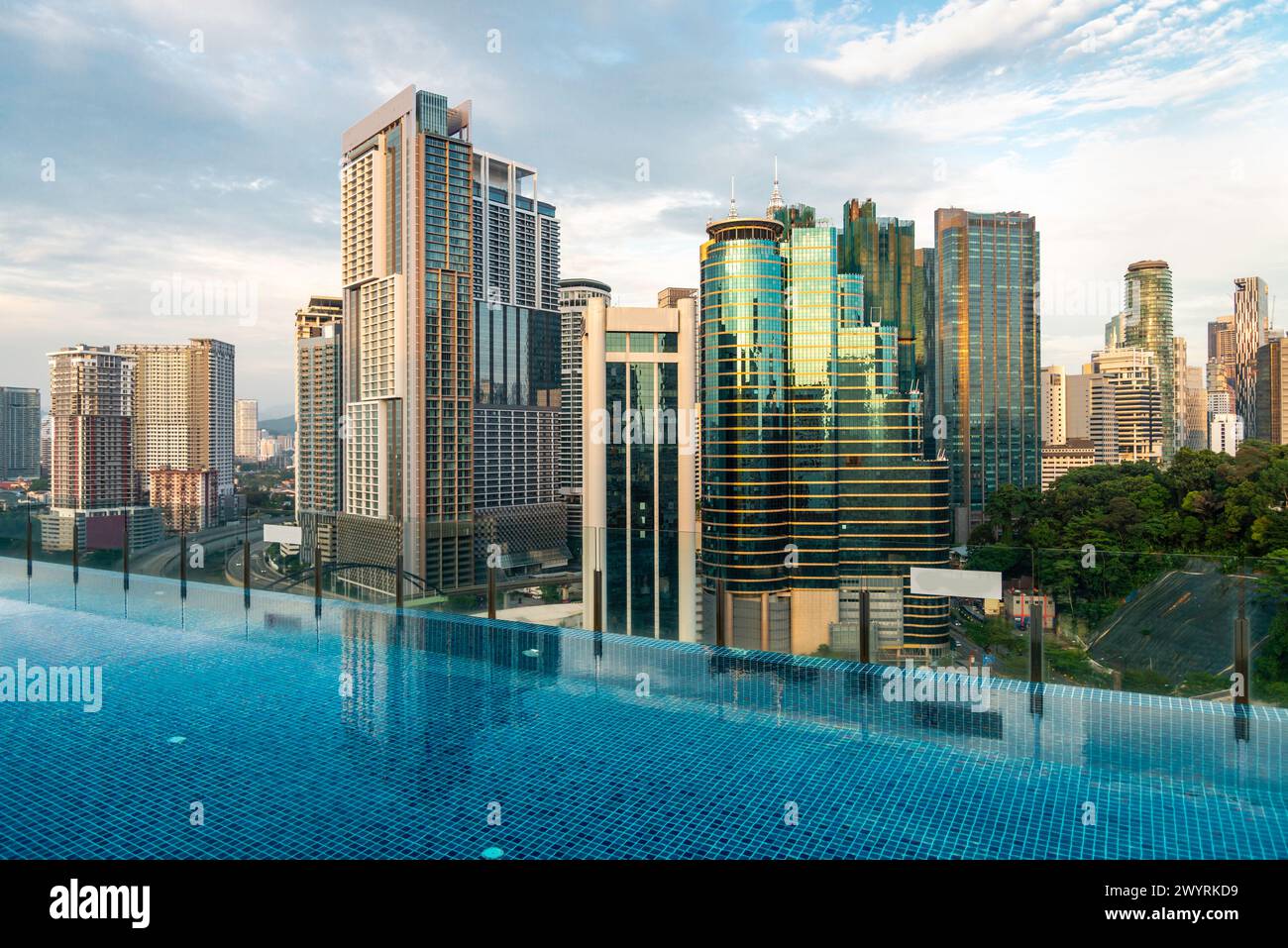 Splendida vista sul tetto della città di Kuala Lumpur e di Menara Kuala Lumpur, vicino al tramonto, con la piscina a sfioro del bar sul tetto blu in primo piano e il cielo blu punteggiato Foto Stock