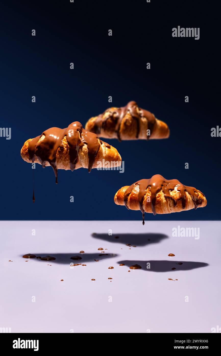Nuvole di croissant ricoperte di cioccolato che fluttuano e gocciolano su sfondo blu Foto Stock
