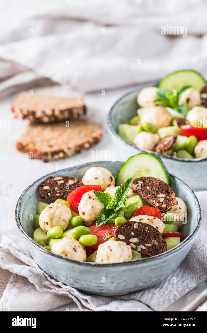 Insalata estiva con cetrioli, mini tomati, mini mozzarella e soia su fondo di legno bianco, verticale Foto Stock