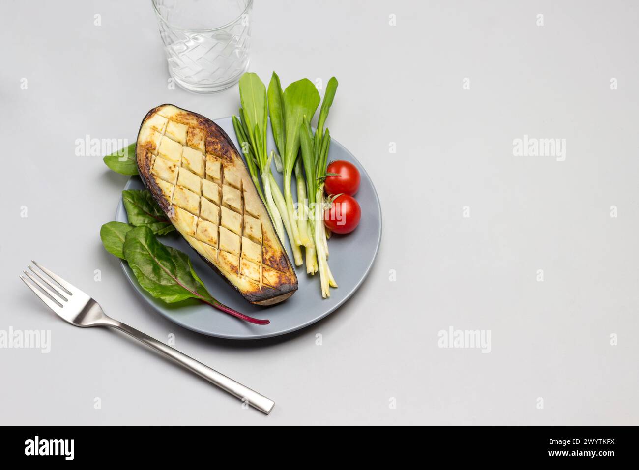 Melanzane grigliate su piatto grigio con pomodori e verdure. Forchetta e due bicchieri. Sfondo grigio. Vista dall'alto. Copia spazio Foto Stock