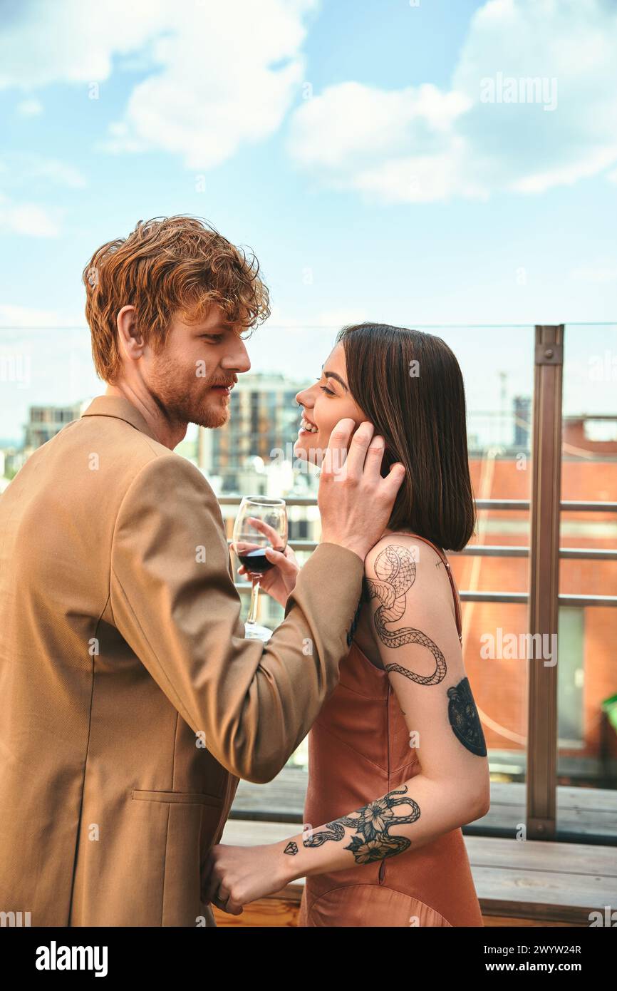 Un uomo e una donna stanno fianco a fianco, la donna che tiene un bicchiere di vino. Sembrano condividere un momento di intimità e connessione Foto Stock