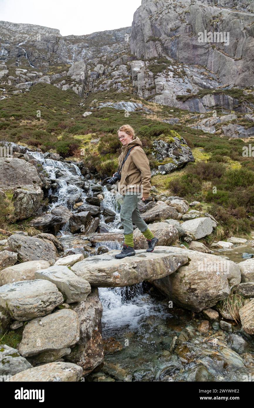 Donna che cammina attraverso il ponte di pietra, il sentiero Llyn Idwal, il parco nazionale Snowdonia vicino a Pont Pen-y-benglog, Bethesda, Bangor, Galles, Gran Bretagna Foto Stock