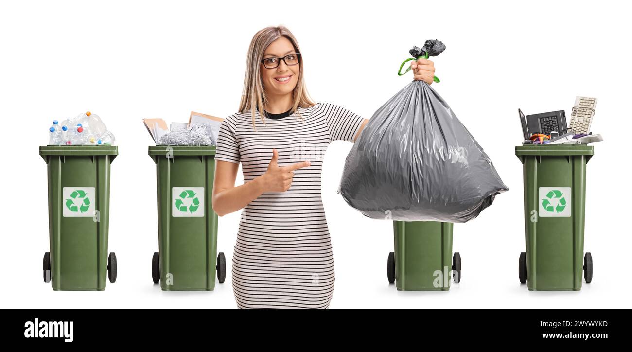 Giovane donna che punta verso un sacchetto di rifiuti davanti a bidoni di riciclaggio isolati su sfondo bianco Foto Stock
