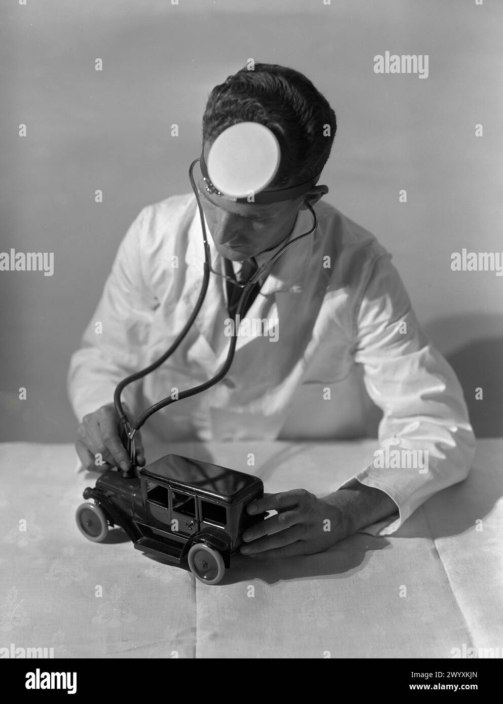 Gordon Burt - Un uomo è umoristicamente raffigurato come uno stetoscopio su una piccola auto giocattolo, indossando uno specchio per la testa comunemente associato ai medici - 1925 Foto Stock