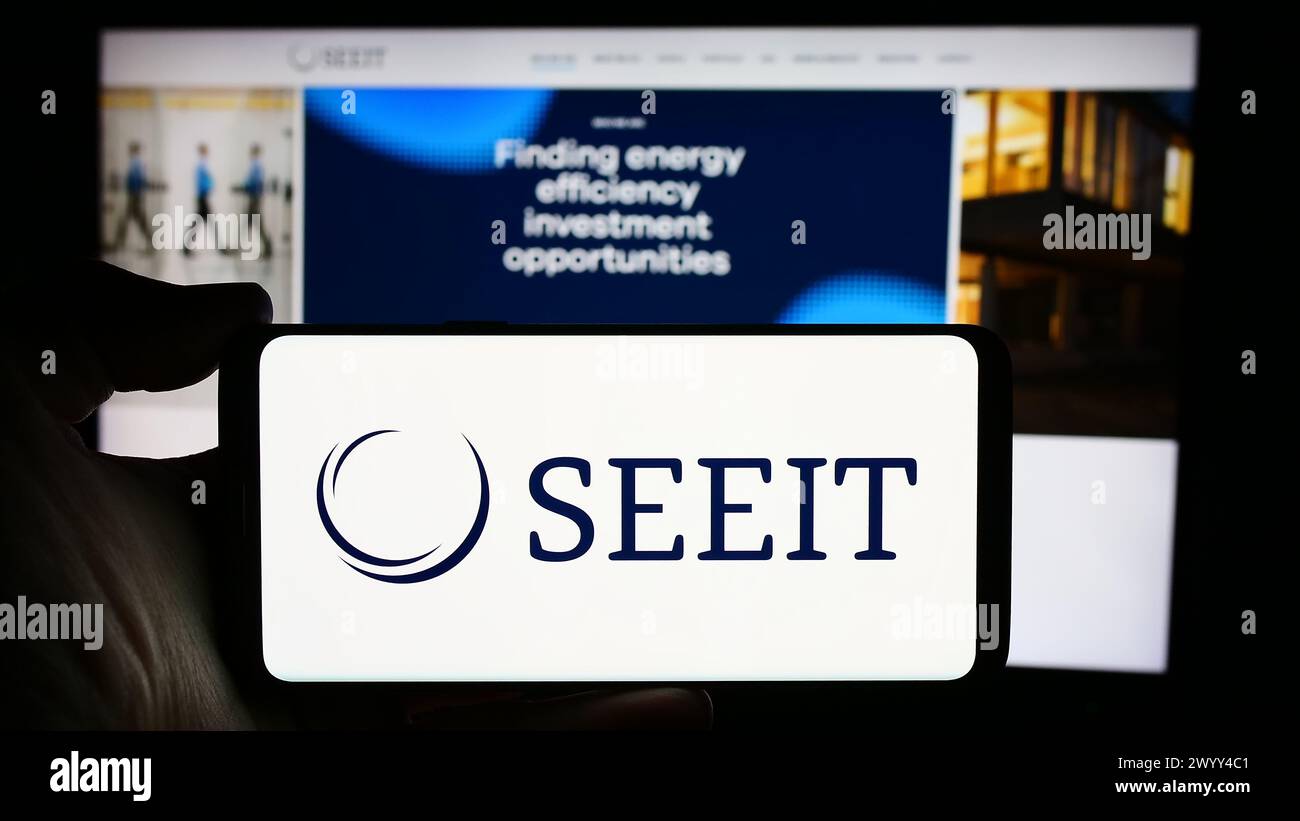 Persona che detiene un cellulare con il logo della società SDCL Energy Efficiency Income Trust (SEEIT) di fronte alla pagina web aziendale. Mettere a fuoco il display del telefono. Foto Stock