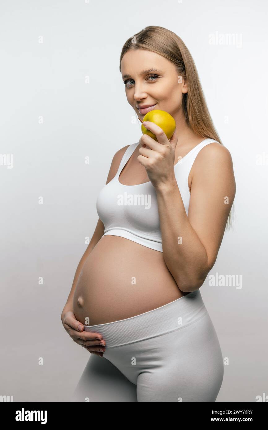 Donna incinta bionda sorridente con mela in mano Foto Stock