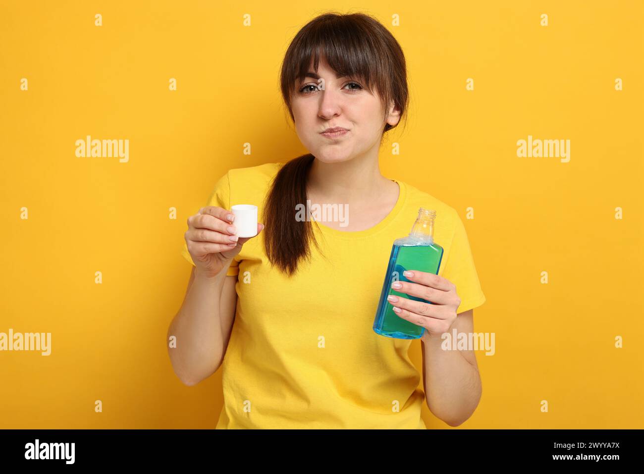 Giovane donna che usa collutorio su sfondo giallo Foto Stock