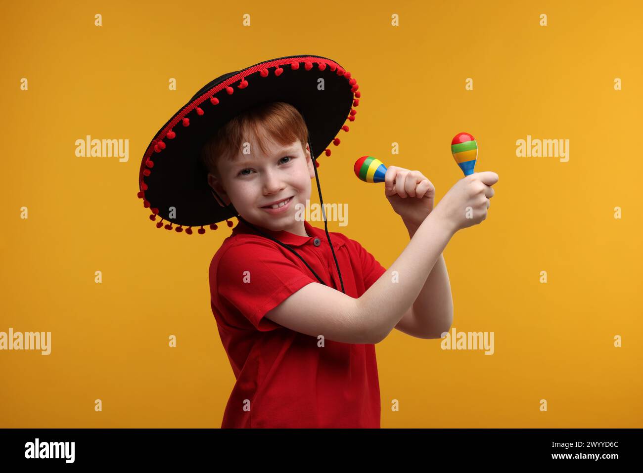 Ragazzo carino con cappello da sombrero messicano con maracas su sfondo giallo Foto Stock