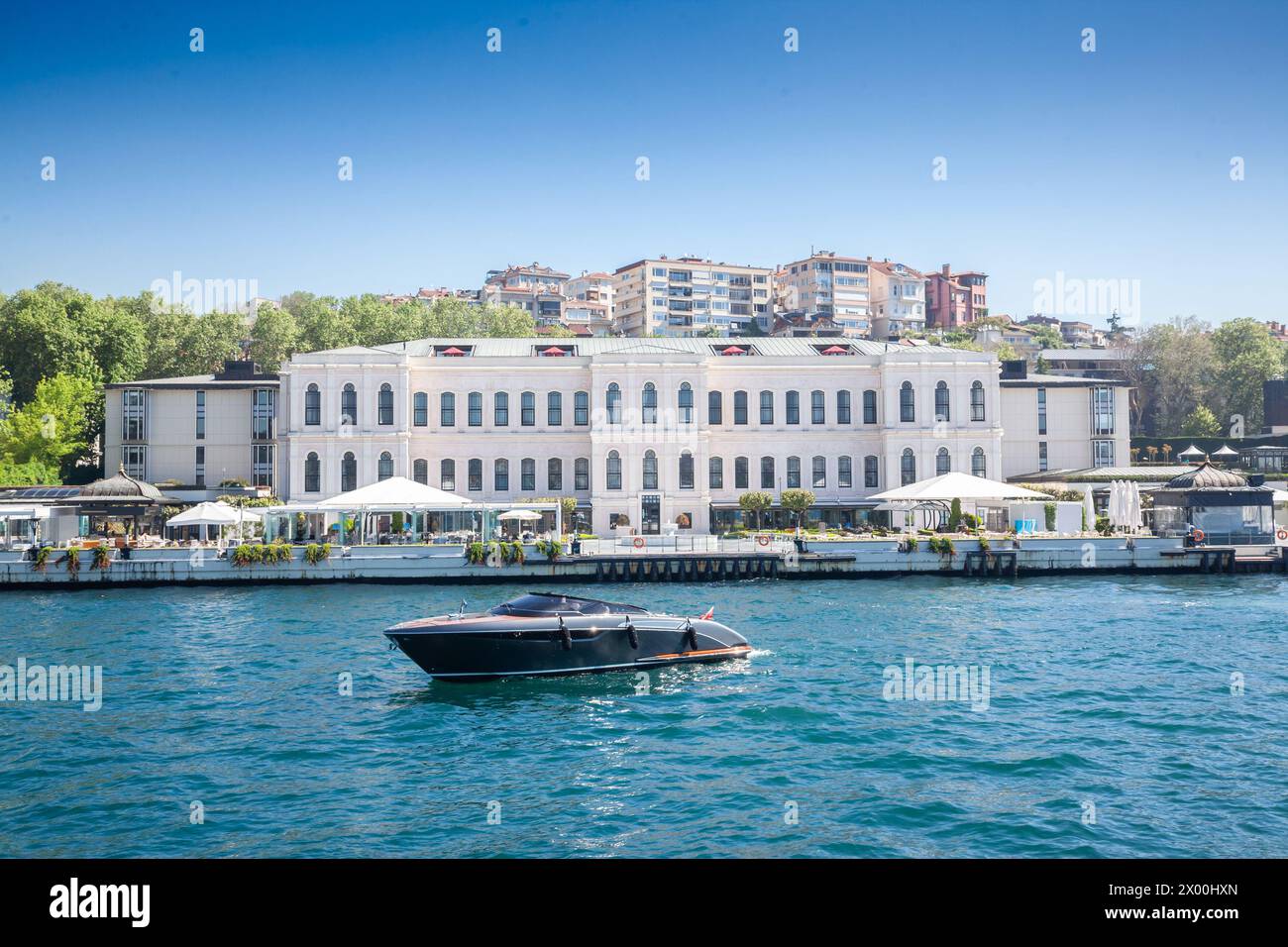 Catturata in una giornata serena, questa vivida immagine di Istanbul presenta un sontuoso yacht che naviga lungo il Bosforo. Dietro di essa, un elegante edificio sul lungomare Foto Stock