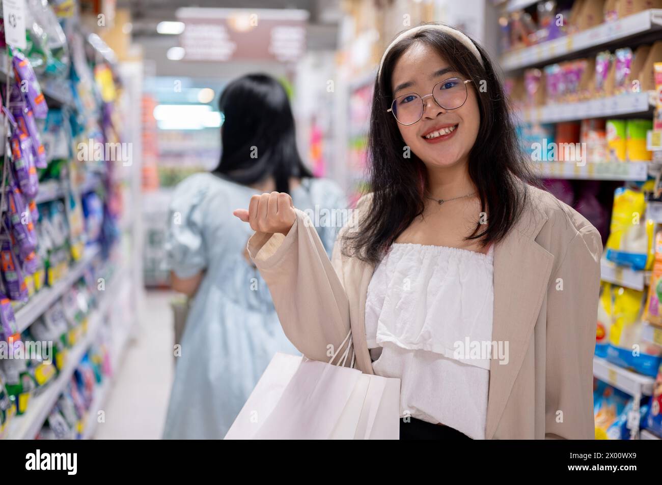 Una giovane donna asiatica sorridente si trova in un corridoio della spesa, tenendo borse della spesa, facendo shopping in un supermercato. concetti di shopping e stile di vita Foto Stock