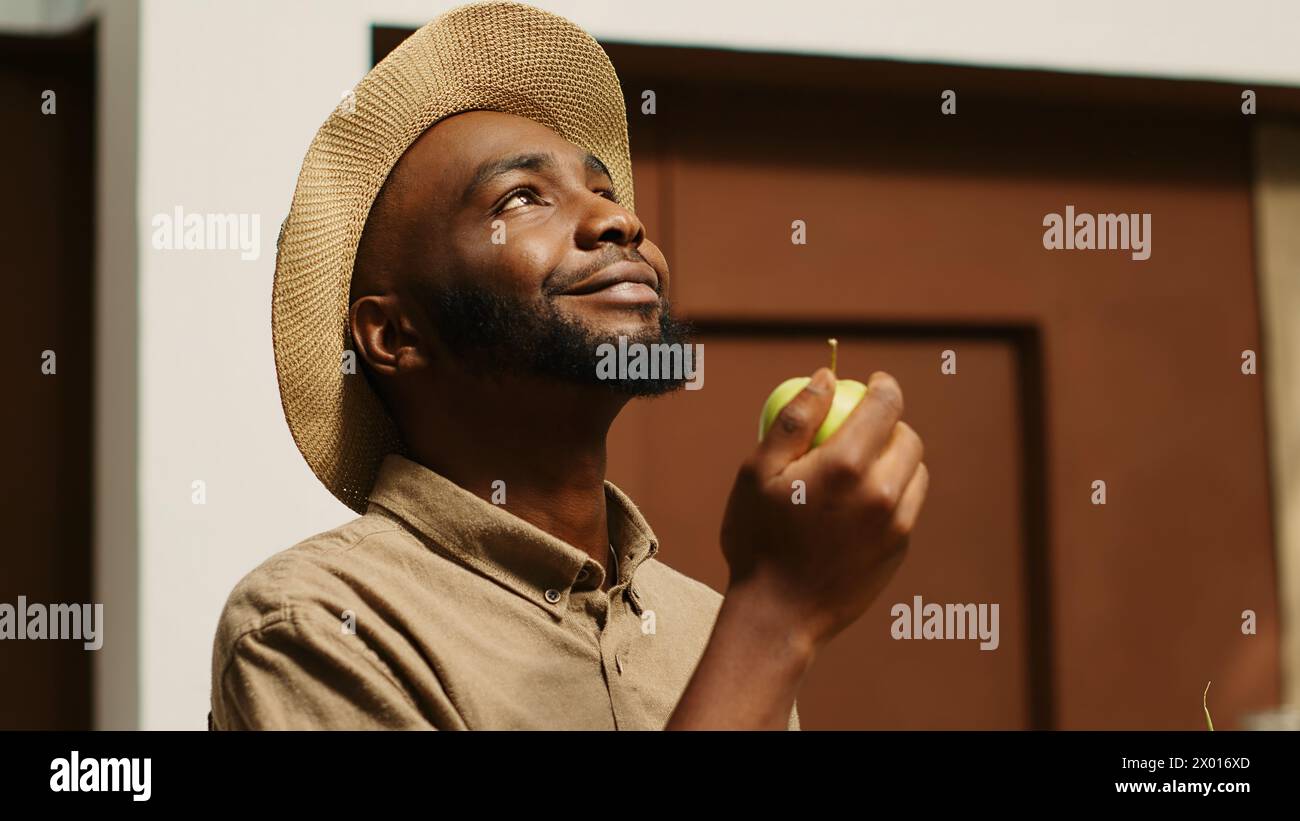 Un uomo afroamericano puzza di mele coltivate localmente al supermercato, sostenendo le piccole imprese non inquinanti acquistando cibo biologico. Il cliente sceglie frutta da casse, godendo di un aroma naturale. Telecamera 1. Foto Stock