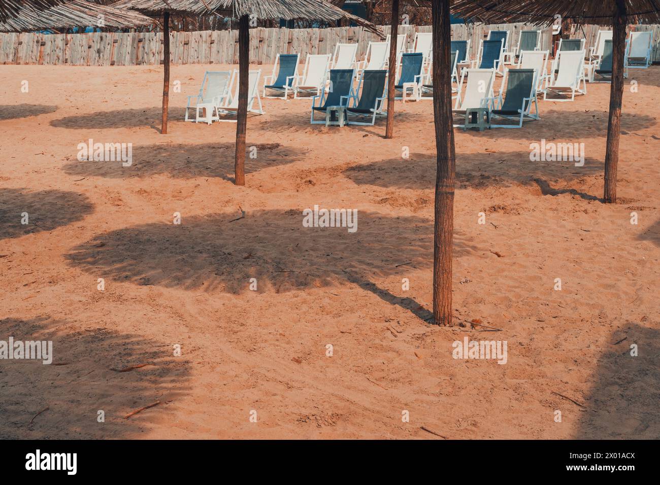 Ombrelloni e sedie a sdraio in paglia di canna sulla spiaggia sabbiosa, concentrazione selettiva Foto Stock