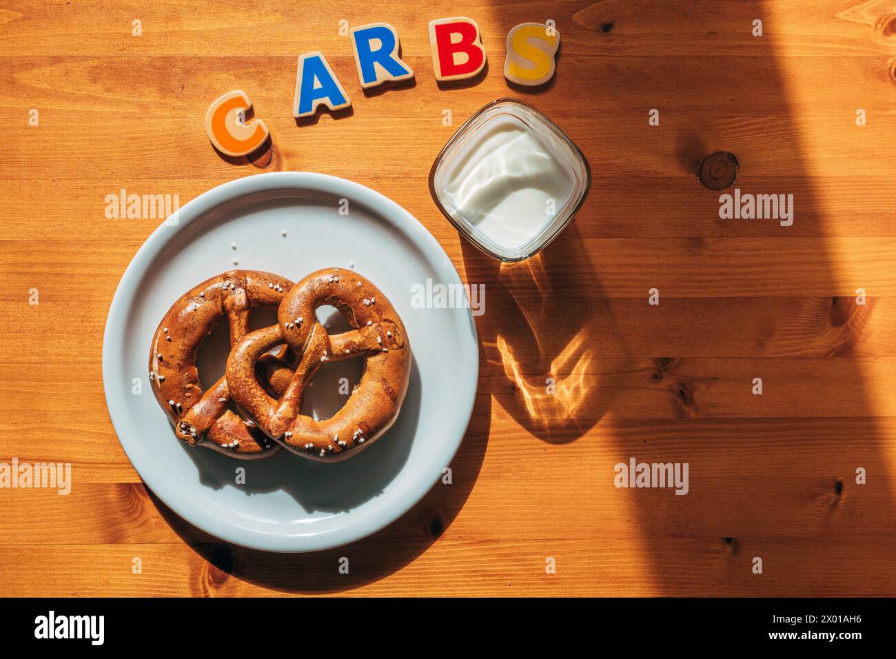 Carboidrati per colazione, bicchiere di yogurt e due pretzel su un piatto sul tavolo al mattino, attenzione selettiva Foto Stock