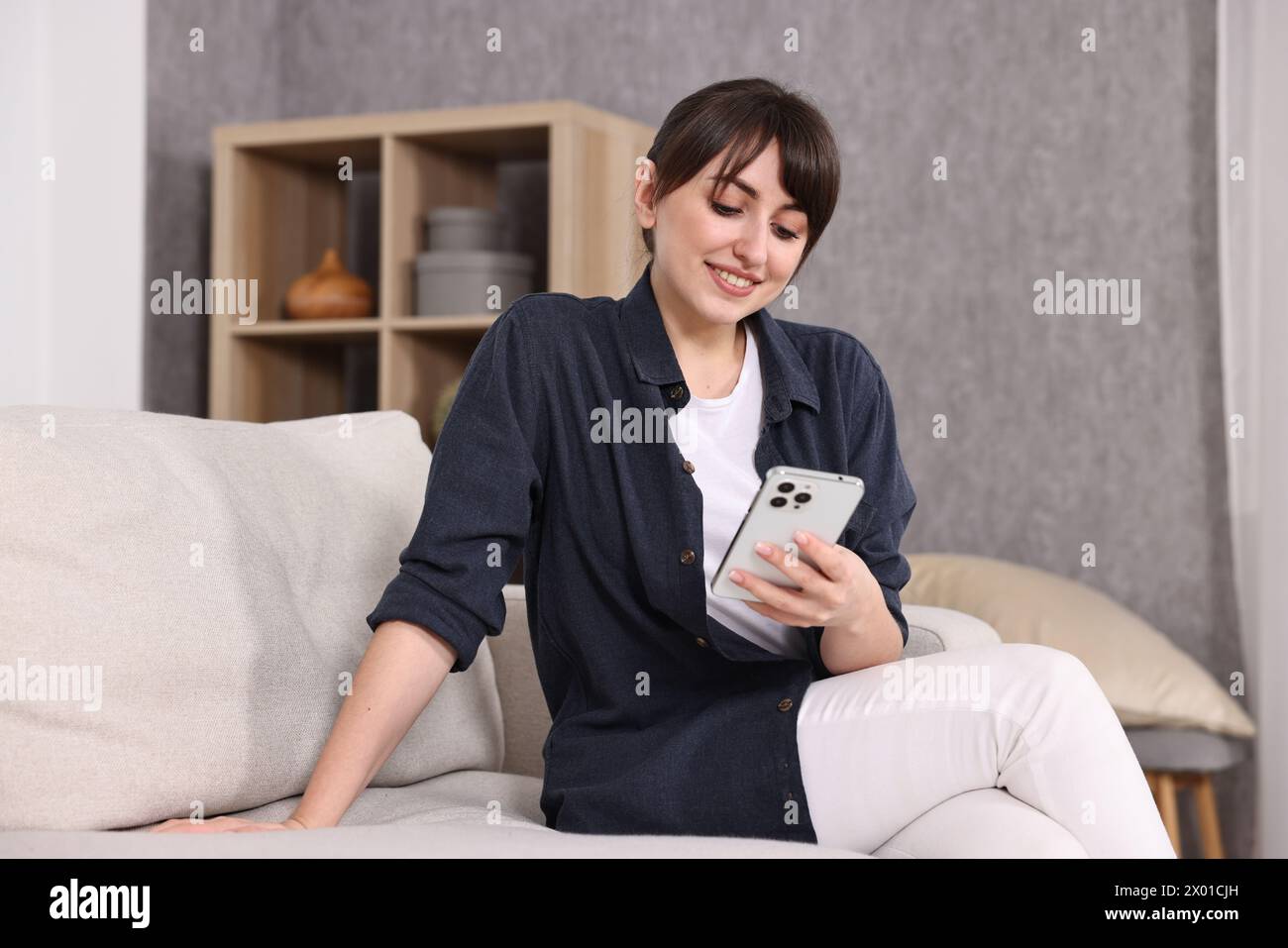 Bella giovane casalinga che usa lo smartphone sul divano di casa Foto Stock