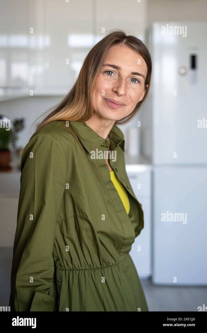Donna scandinava di mezza età sorridente con un'espressione piacevole che guarda la macchina fotografica nella cucina di casa Foto Stock
