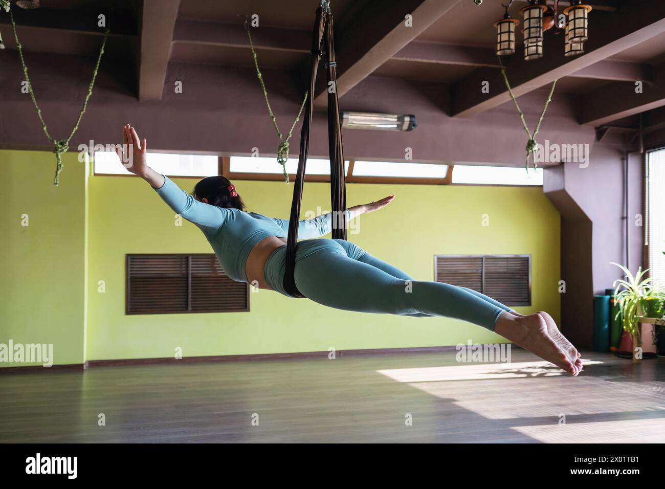 Donna che esegue l'asana dell'equilibrio in un'amaca, Sarpasana, posa serpente, allenamento da sola in abbigliamento sportivo, concetto di yoga aereo Foto Stock