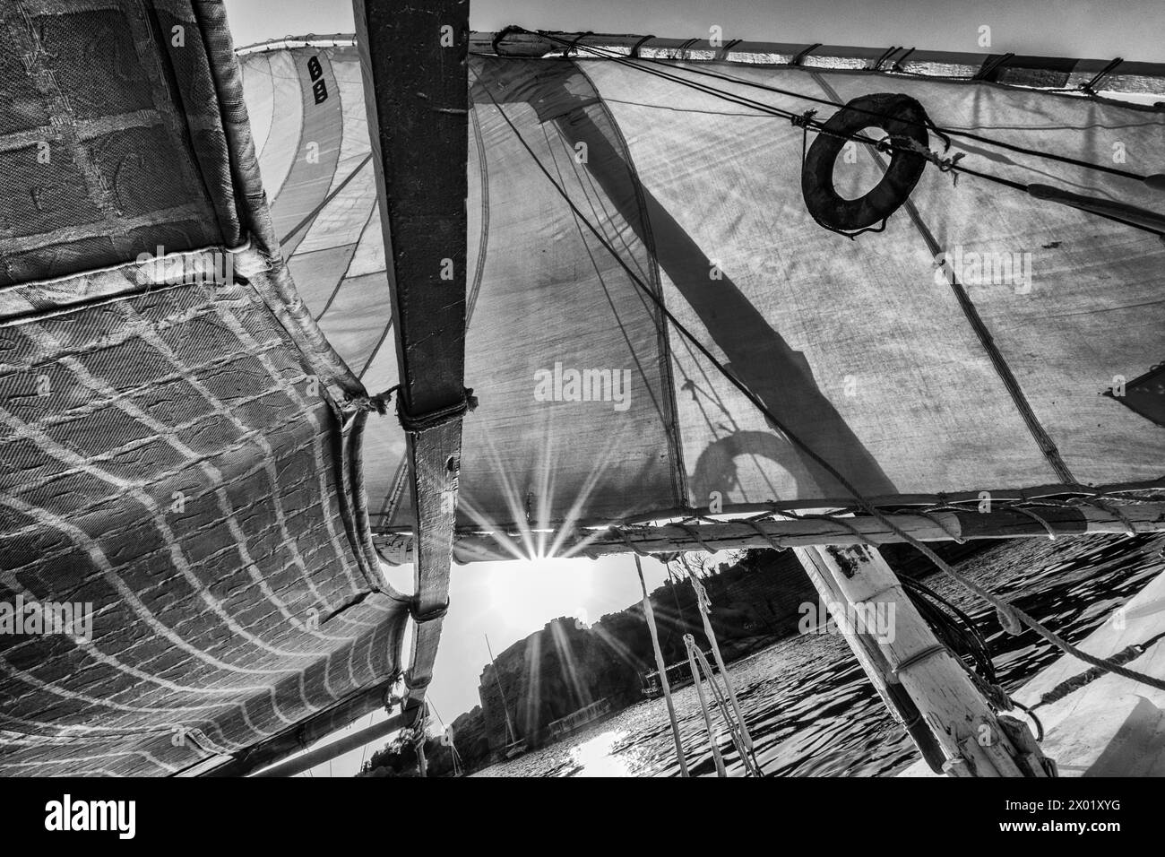 Una vista filtrata in bianco e nero del sole che splende attraverso l'attrezzatura e la vela su una feluca egiziana o una barca a vela sul Nilo ad Assuan. Foto Stock