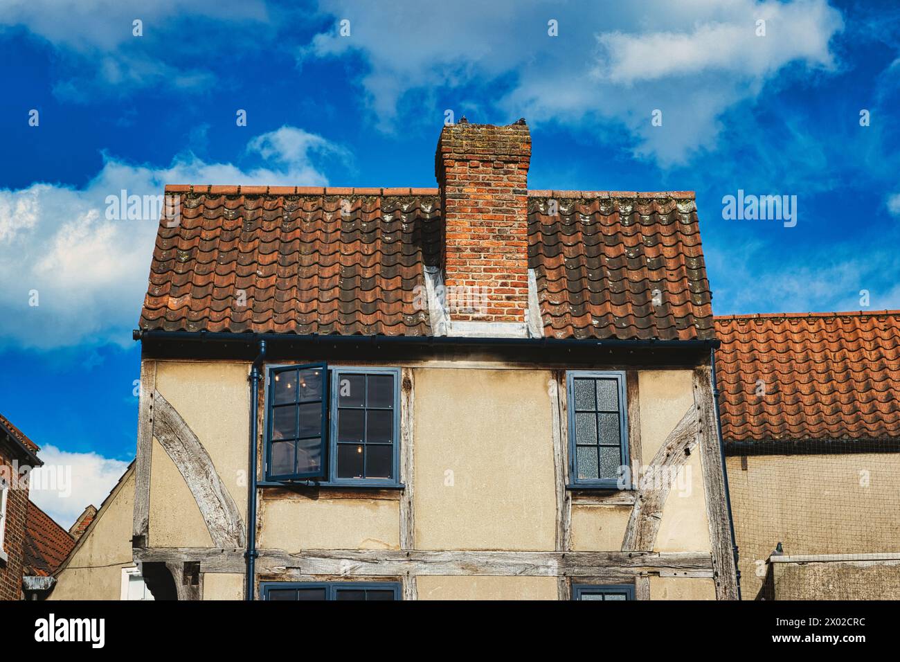 Vecchia casa europea con pareti a graticcio e un tetto di tegole rosse su un cielo blu con nuvole. Architettura d'epoca con vestibilità e carattere visibili Foto Stock