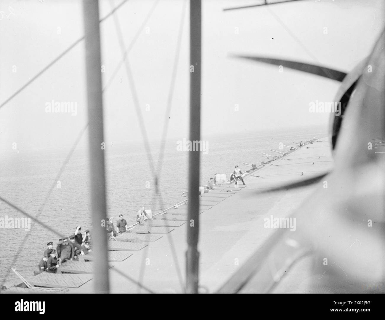 IL PESCE SPADA FAIREY ATTERRA SU UNA PORTAEREI DI SCORTA. DAL 20 AL 23 LUGLIO 1943, IN MARE, A BORDO DEL FAIREY SWORDFISH MENTRE ATTERRA SULLA PORTAEREI DI SCORTA, HMS ACTIVITY. - Atterrare sul piccolo ponte del vettore. Il naso del Fairey Swordfish è tenuto in alto, in modo che il gancio alla coda dell'aereo raccolga uno dei fili di arresto che possono essere visti allungati sul ponte. L'ufficiale "Bats" che controlla l'atterraggio sta dando un segnale al pilota di scendere un po', mentre sulla sinistra l'equipaggio di manovra nelle reti laterali si sta preparando a saltare sull'aereo non appena Foto Stock