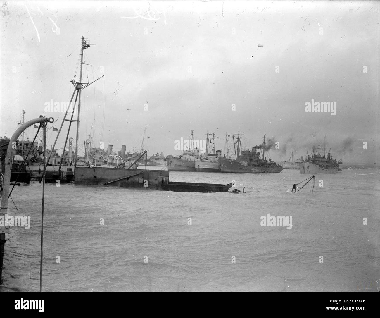 Tra il 12 e il 15 giugno 1944, uno dei porti britannici di Mulberry iniziò le operazioni ad Arromanches. Varie navi riparate durante una burrasca, con una nave affondata visibile in primo piano. Foto Stock
