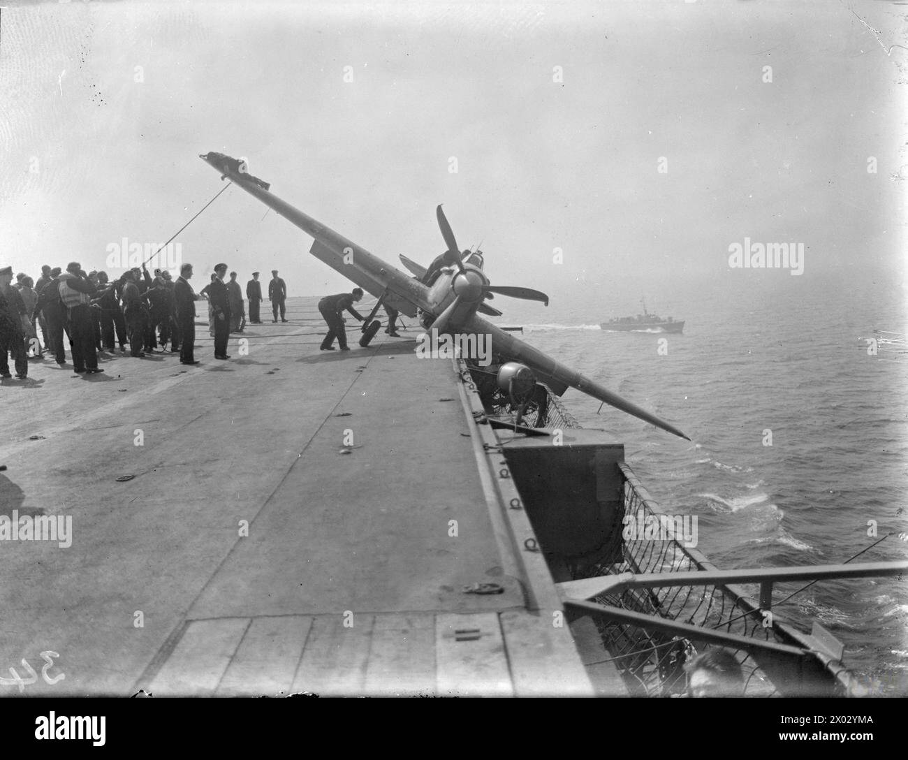 Il 15–17 agosto 1943, la HMS Argus, al largo di Lamlash, celebrò 25 anni di servizio mentre addestrava i piloti della Fleet Air Arm ad atterrare sulle portaerei. Un aereo viene mostrato intrappolato nelle reti con un lancio di salvataggio sullo sfondo. Foto Stock