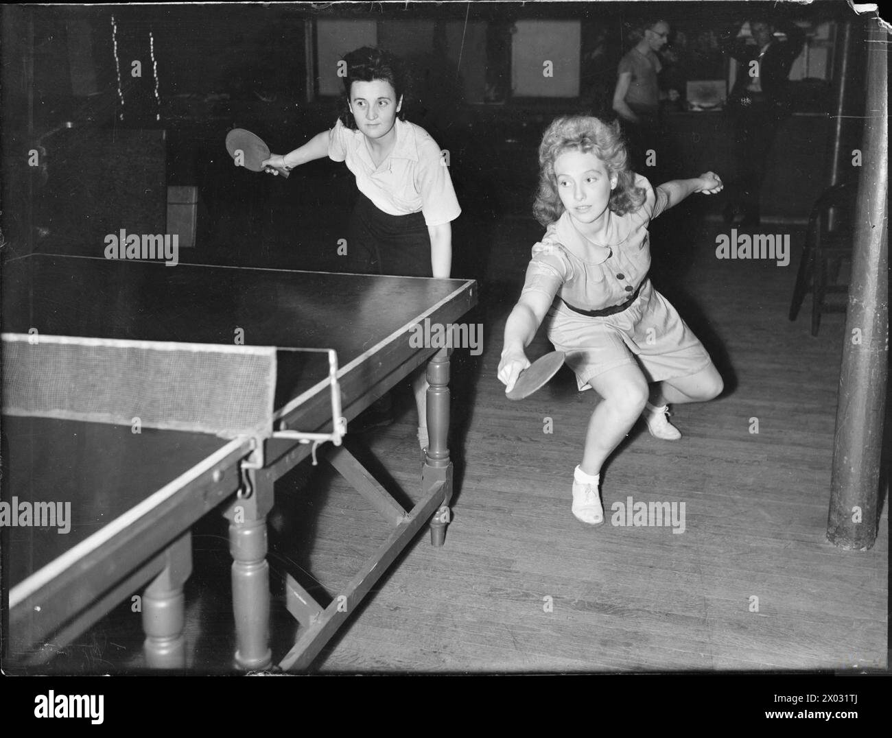 VACANZE A CASA: DIVERTIMENTO E RELAX IN TEMPO DI GUERRA A LONDRA, INGHILTERRA, 1943 - Pinkie Barnes e Peggy Franks competono in una partita di ping-pong da due donne. Peggy ha appena fatto un basso ritorno indietro Foto Stock