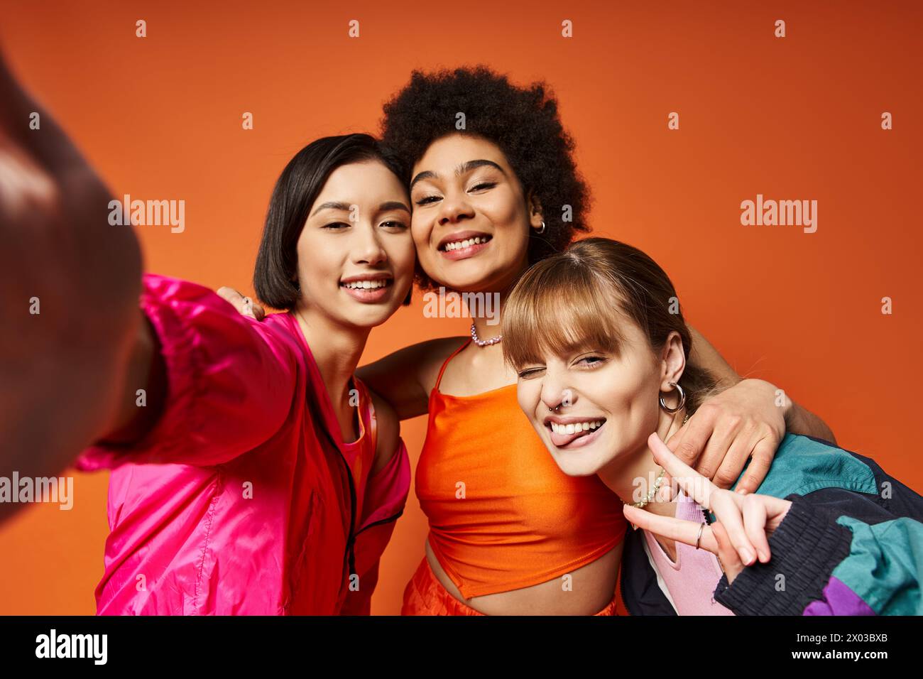 Un gruppo di donne diverse che catturano momenti con un cellulare su uno sfondo arancione. Foto Stock