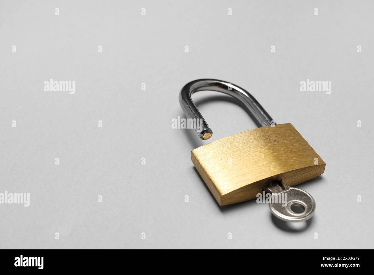Lucchetto in acciaio con chiave su sfondo grigio, primo piano. Spazio per il testo Foto Stock
