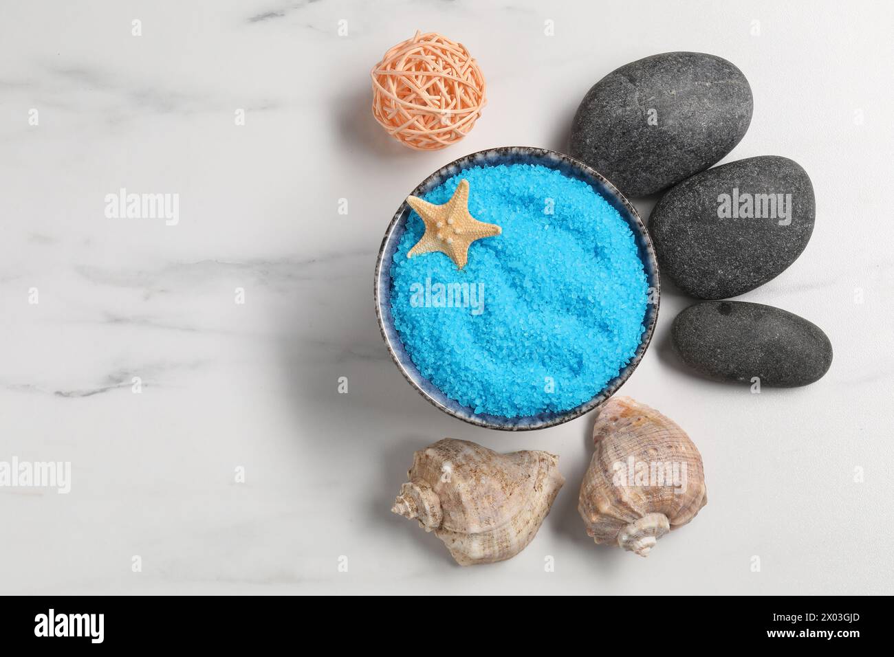 Sale marino azzurro in ciotola, pietre termali, stelle marine e conchiglie su un tavolo in marmo bianco, piano. Spazio per il testo Foto Stock