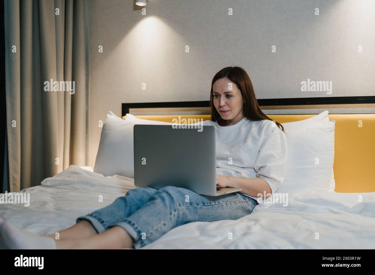 Donna rilassata impegnata a utilizzare il proprio computer portatile mentre si sdraia comodamente sul letto, si telelavoro o si diverte a divertirsi. Foto Stock