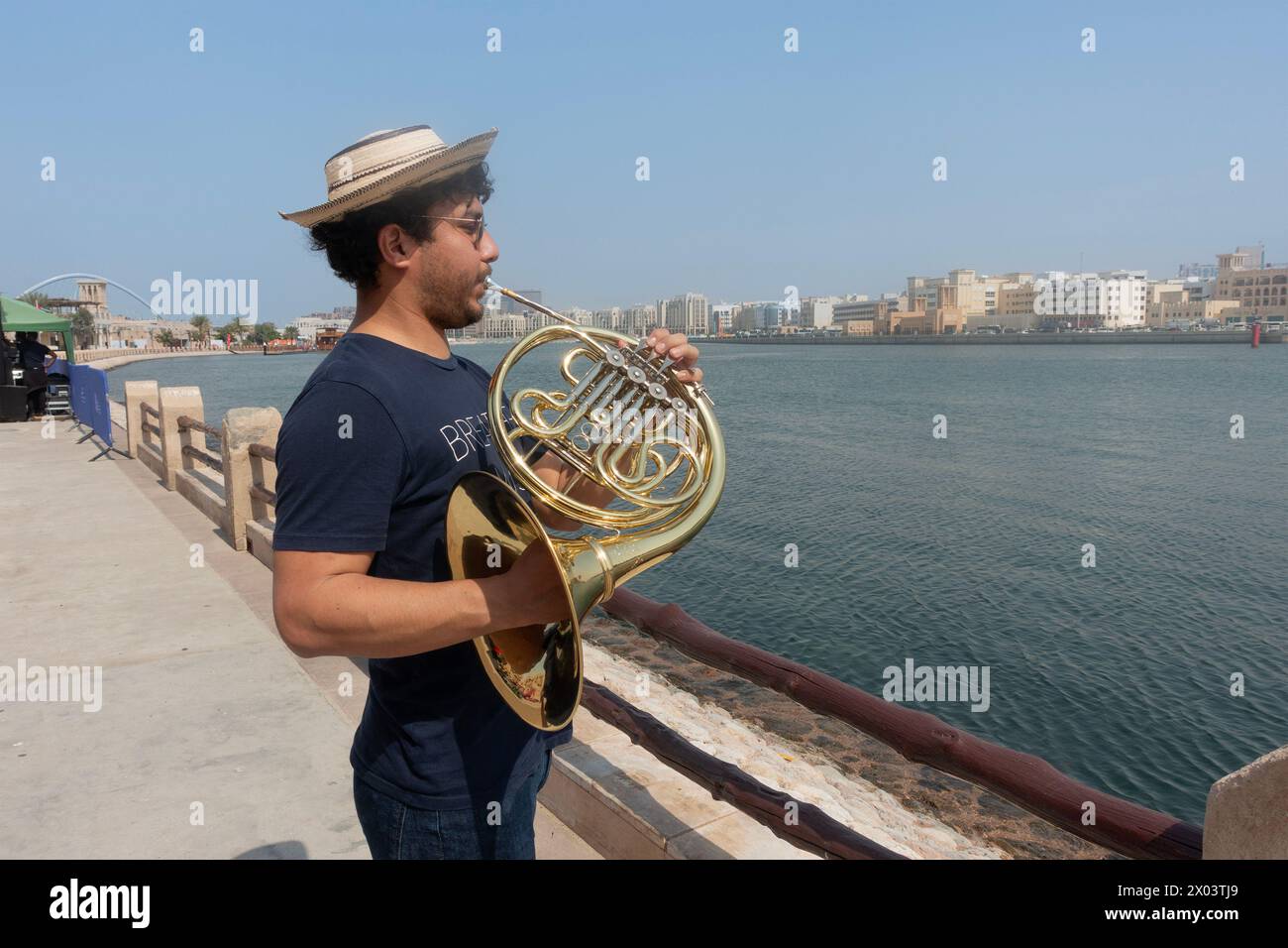 Giovane musicista che suona il corno francese sulla riva del torrente nel quartiere storico di al Shindagha, Dubai, Emirati Arabi Uniti. Foto Stock